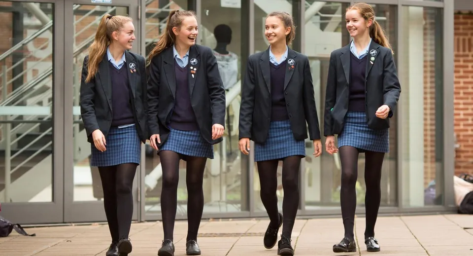 Quattro studentesse della Headington School sono insieme davanti a un edificio in vetro e sorridono.
