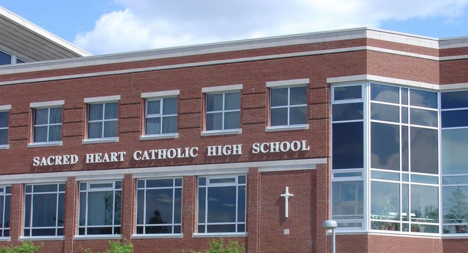 Il grande edificio in mattoni della Sacred Heart High School è visibile sotto un cielo blu limpido con nuvole.