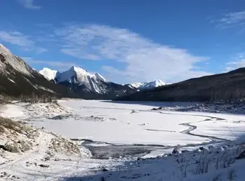 Lago helado en un valle rodeado de montañas nevadas bajo un cielo azul