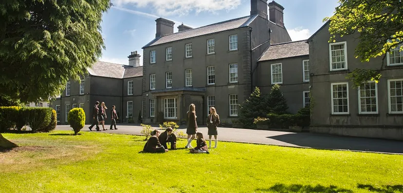 Studenti in uniforme scolastica sono seduti e in piedi sul prato davanti all'edificio storico della Royal School Dungannon.