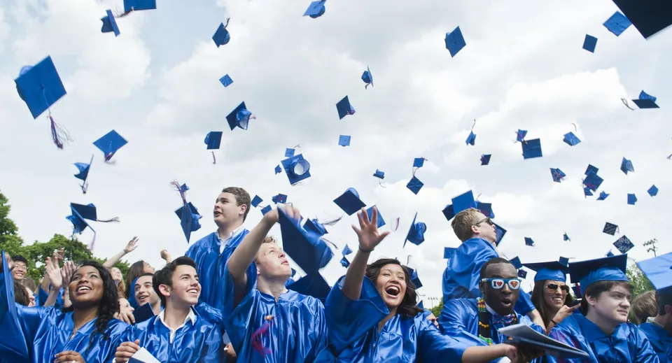 I laureati del Queensbury Union Free School District lanciano i loro tocchi in aria durante la cerimonia di diploma sotto un cielo nuvoloso.