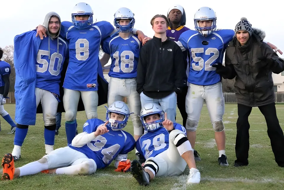 Un gruppo di giovani calciatori in maglia blu sul campo da gioco della Oak Park High School con spettatori sullo sfondo.
