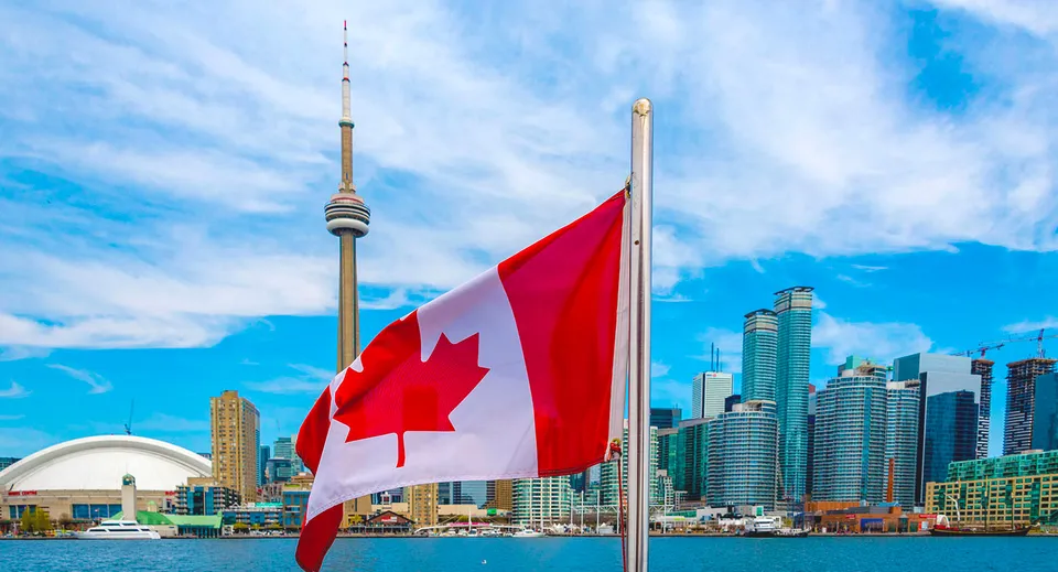 Una grande bandiera canadese sventola sul campus del Woburn Collegiate Institute davanti allo skyline di Toronto con la CN Tower.