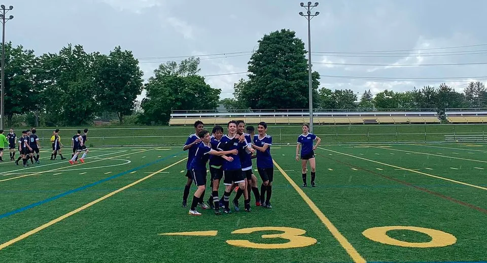 Un gruppo di studenti della Dr. G.W. Williams Secondary School si raduna su un campo sportivo accanto a uno stadio.