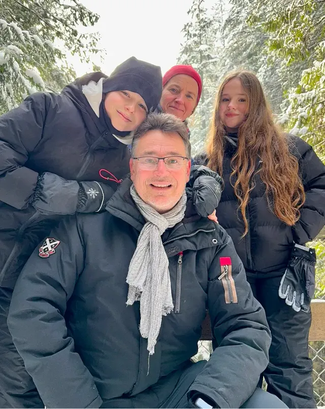 Famiglia ospitante di quattro persone in abbigliamento invernale sorride tra alberi innevati