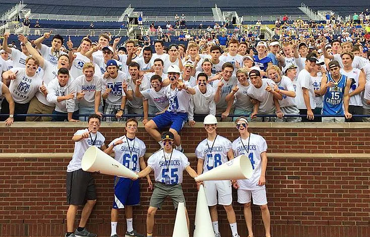 Estudiantes de Catholic Central High School se reúnen en las gradas del estadio con megáfonos de cheerleading.