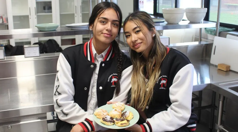 Due studentesse della Rockingham Senior High School sono in piedi in una cucina e tengono un piatto con dei dolci.