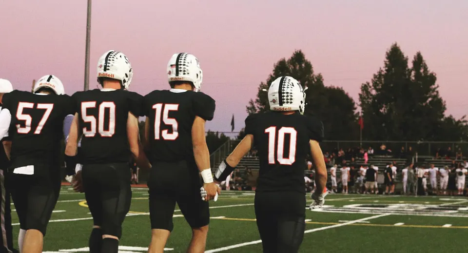 Un gruppo di giocatori di football della Justin Siena High School sta sul campo da gioco al tramonto.