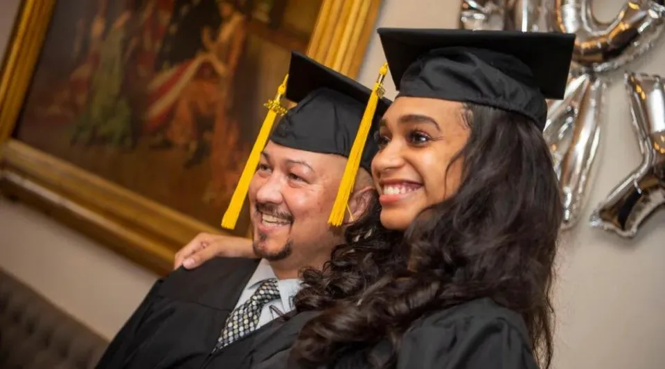Un uomo più anziano e una donna più giovane in abito da diploma posano insieme alla cerimonia di diploma della Georgetown District High School.