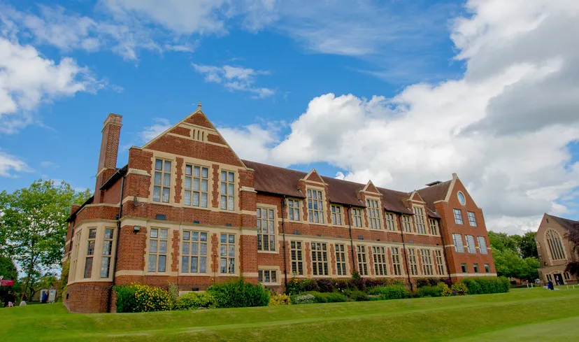 L'edificio storico in mattoni della Bromsgrove School sorge su un prato verde sotto un cielo blu.