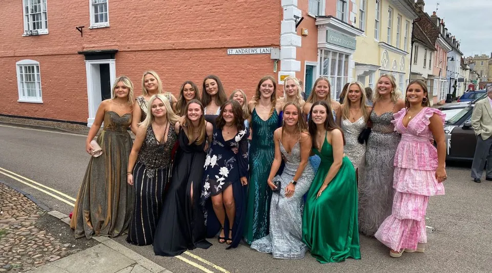 Un gruppo di giovani donne in abito da sera posa in strada davanti a case colorate nel campus della Kimbolton School.
