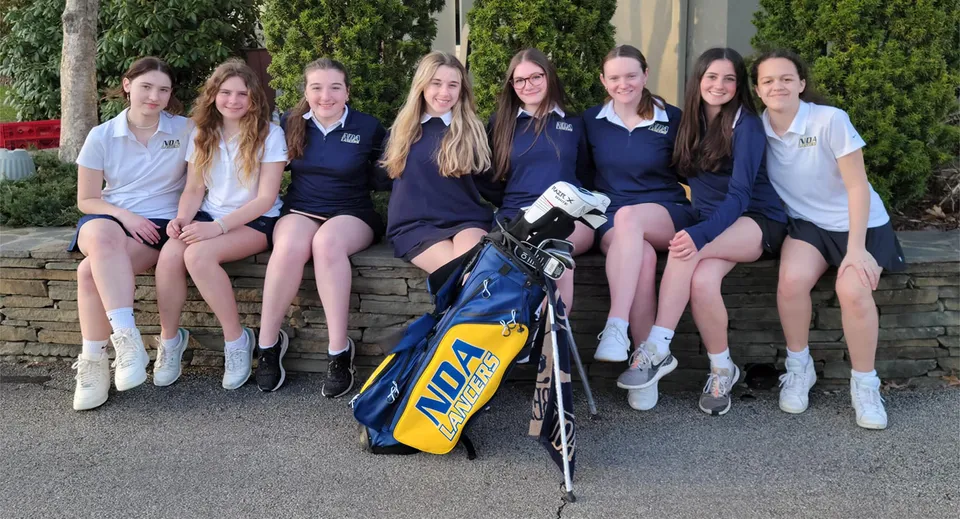 Studentesse della Academy of Notre Dame siedono insieme su un muretto con una sacca da golf in primo piano.