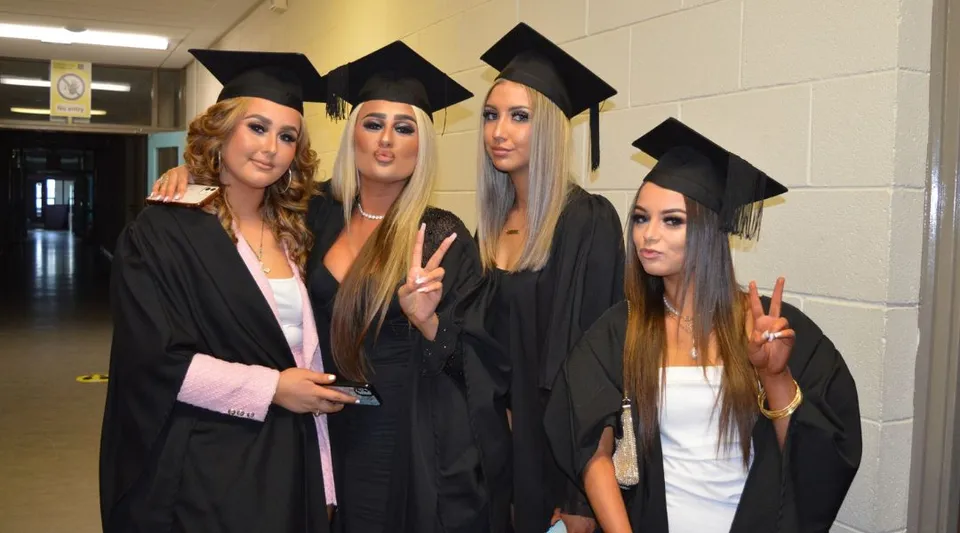 Quattro studentesse in abito da diploma posano insieme nel corridoio dell'Athy College.
