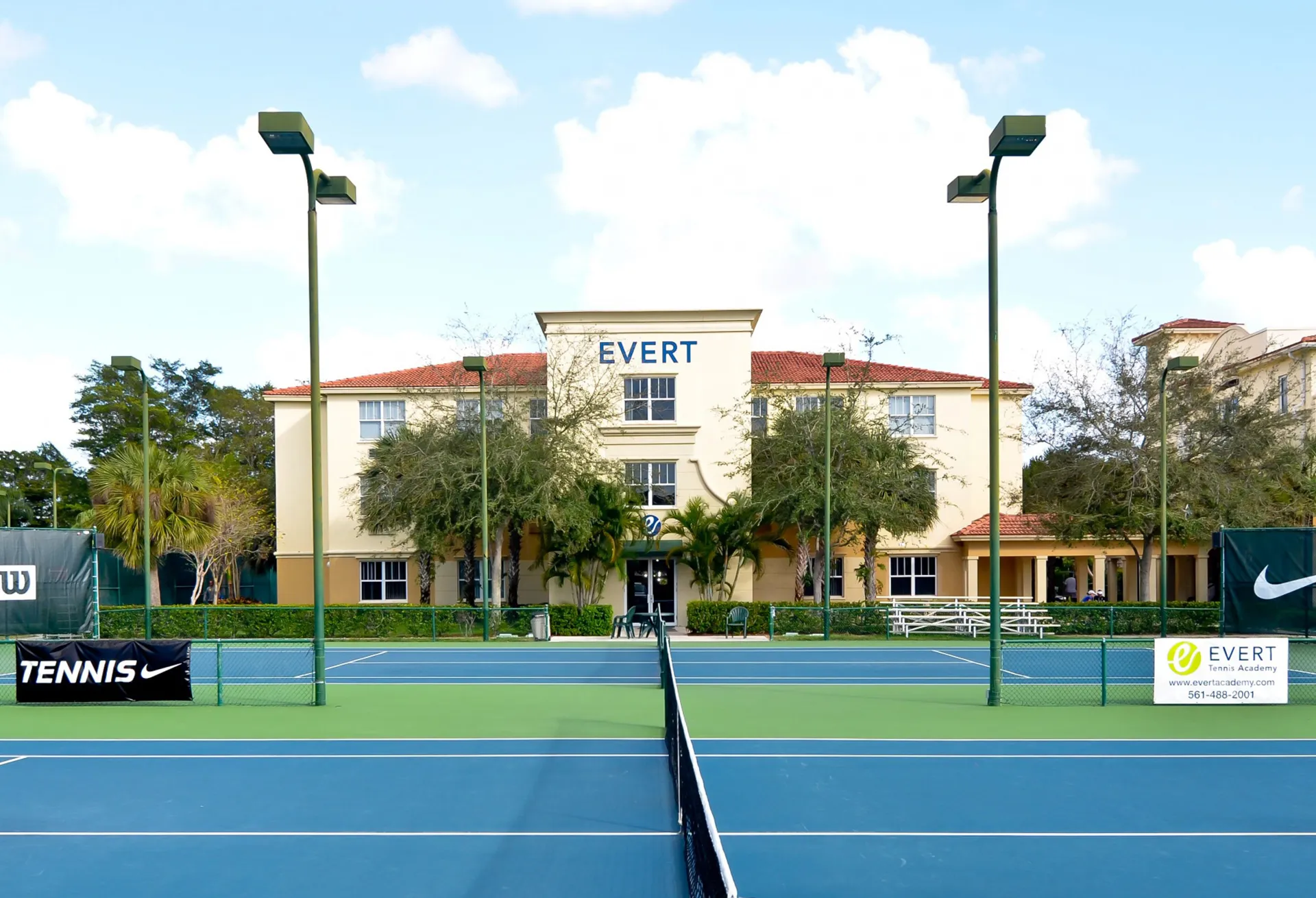 Un campo da tennis blu in primo piano e l'edificio principale della Evert Tennis Academy sullo sfondo.