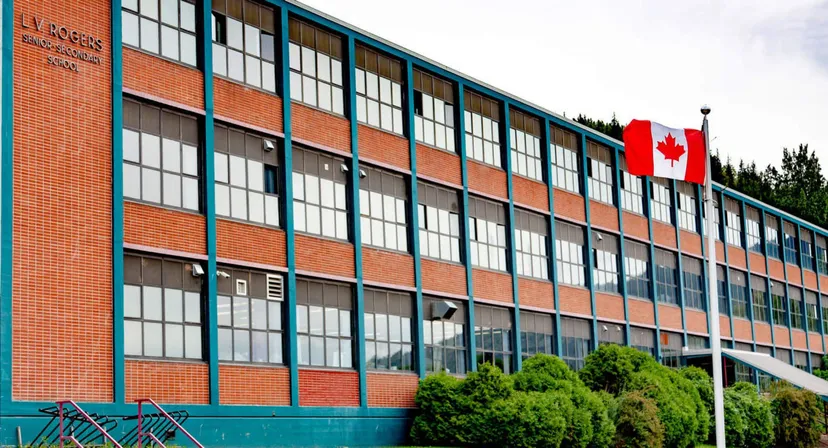 L'edificio in mattoni della L.V. Rogers Secondary School con grandi finestre e una bandiera canadese davanti agli alberi.