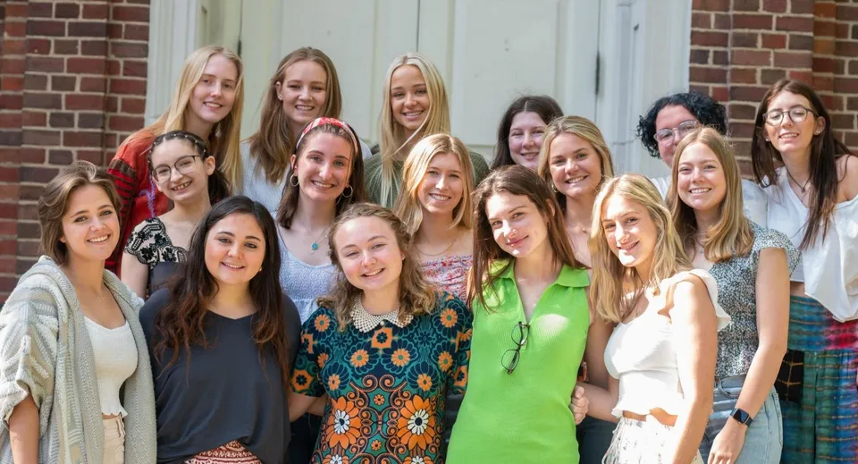 Un gruppo di studentesse sorridenti si trova insieme davanti a un edificio in mattoni nel campus della Chatham Hall School.