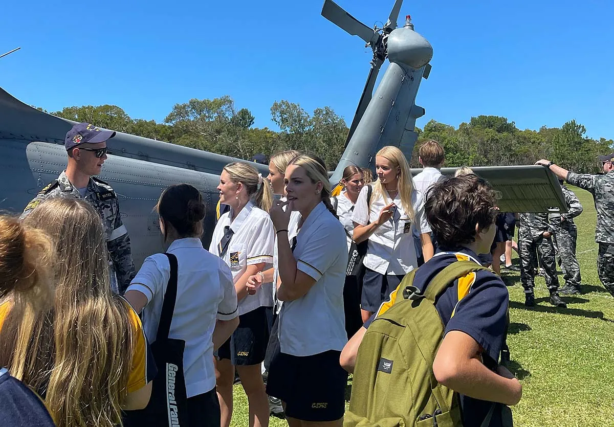 Schülerinnen und Schüler in Schuluniform vor einem Militärhubschrauber mit Soldaten