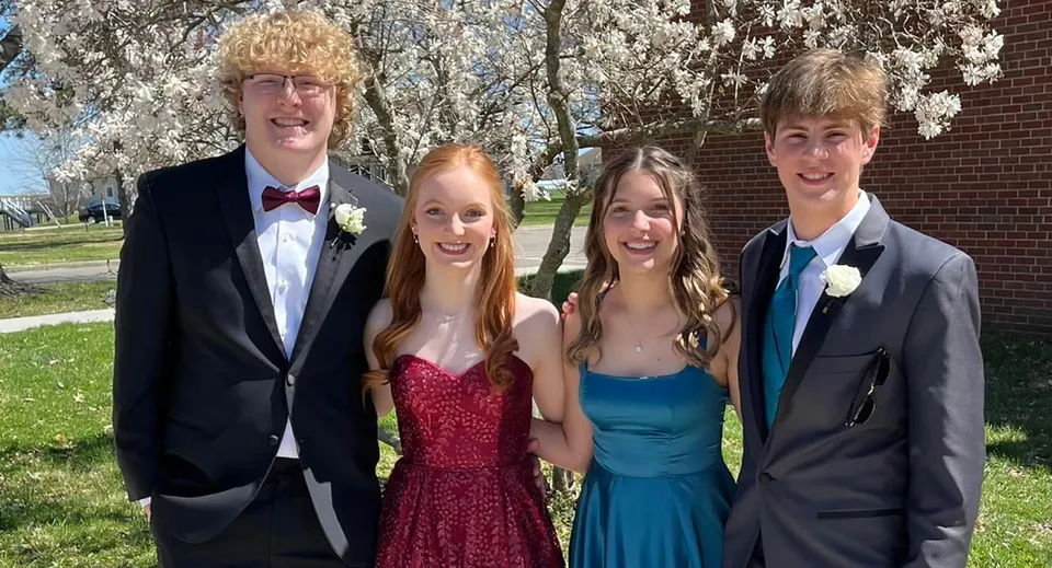 Quattro studenti della Saint Paul Lutheran High School sono insieme in abiti eleganti in un parco con alberi in fiore.
