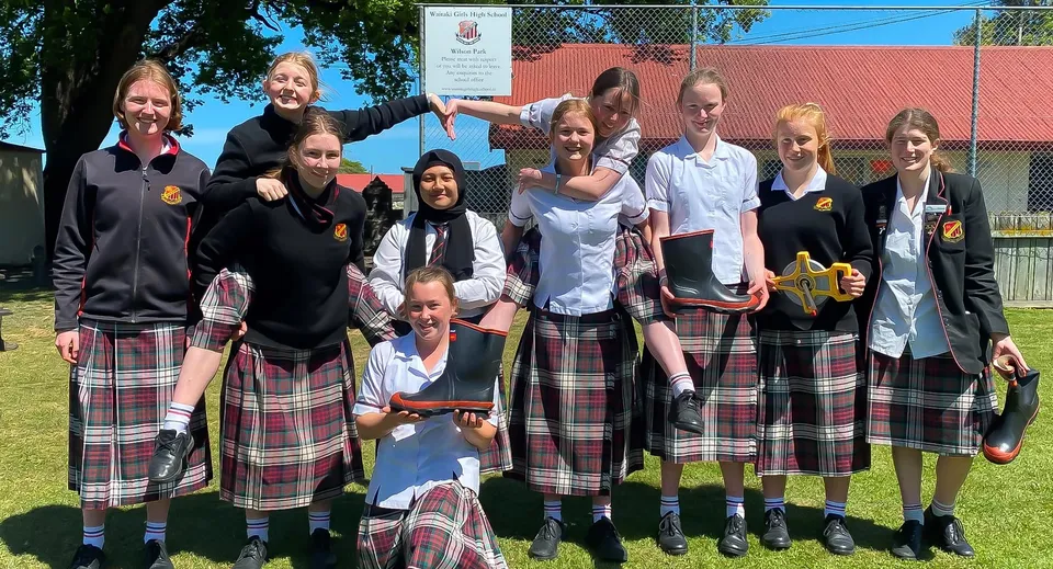 Un gruppo di studentesse della Waitaki Girls’ High School si trova insieme su un prato davanti a un edificio con il tetto rosso.