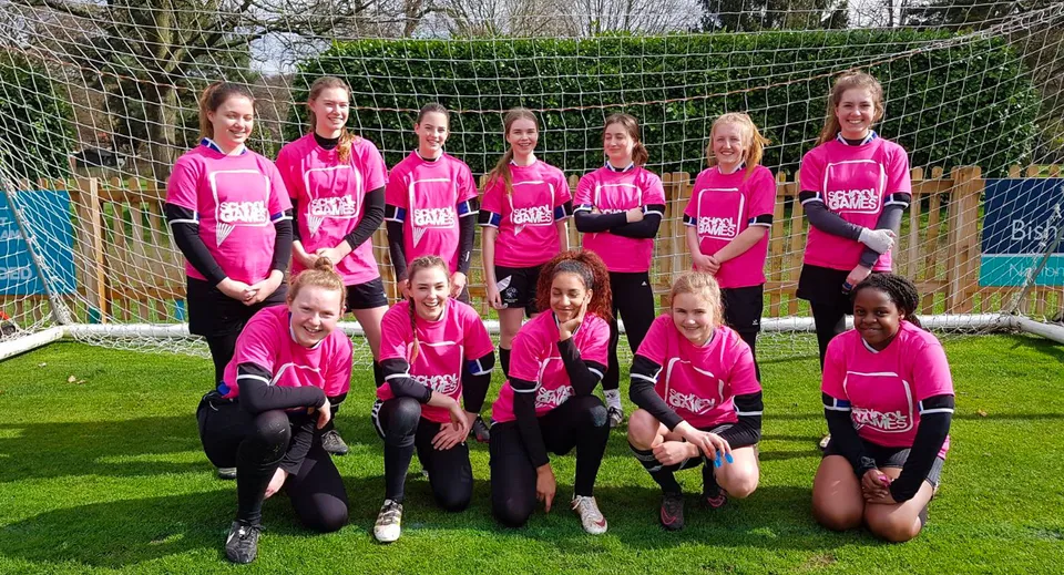 Un gruppo di giovani calciatrici in maglia rosa gioca sul campo sportivo della Denefield School.