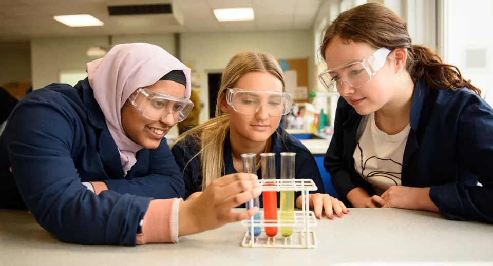Tre studentesse del Portsmouth College esaminano concentrate uno strumento scientifico in laboratorio.