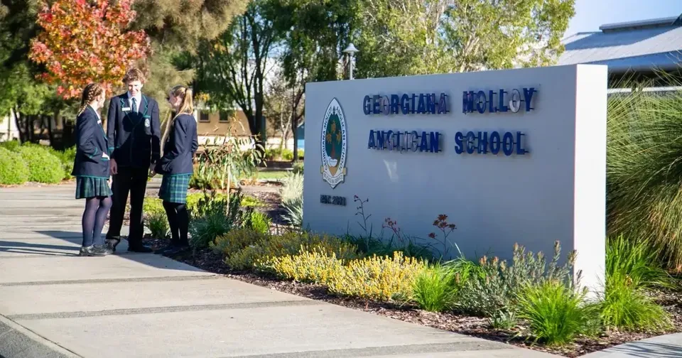 Tre studenti in uniforme scolastica parlano accanto all'insegna della Georgiana Molloy Anglican School.