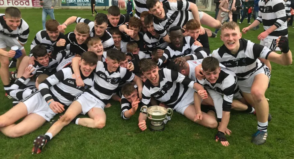 Studenti del Presentation College Carlow festeggiano su un campo con una coppa in mano.