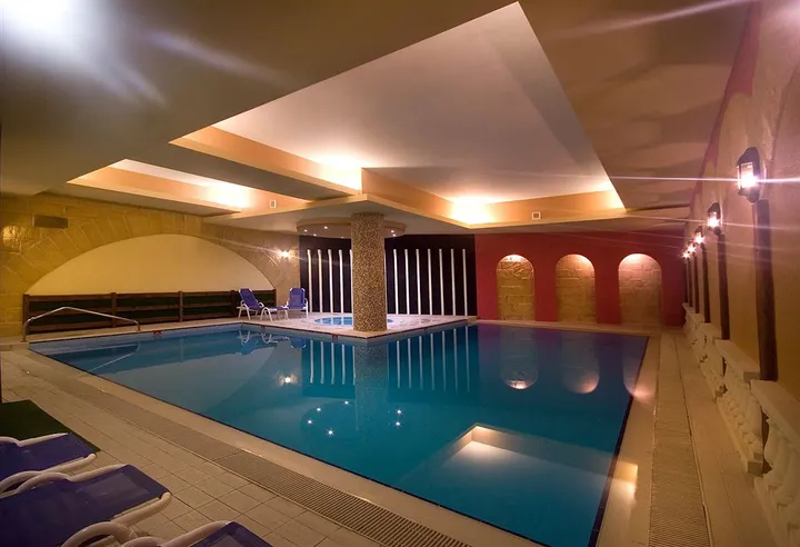 Piscina coperta dell'hotel con lettini blu, archi rossi illuminati e soffitto a volte