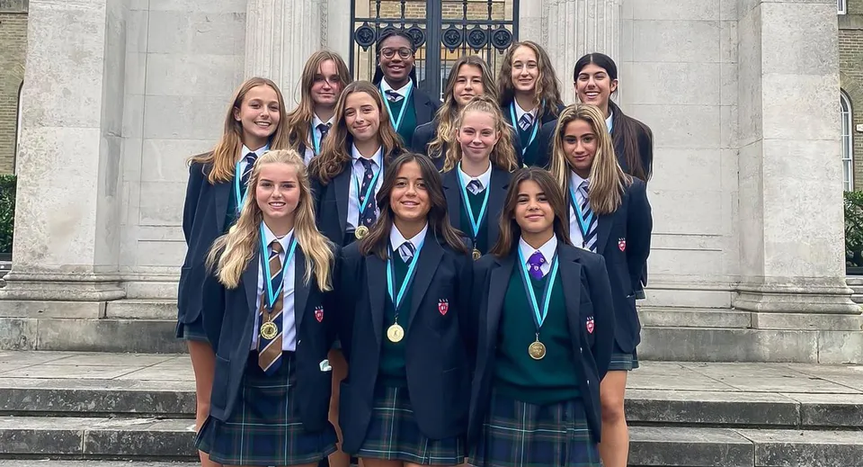 Un gruppo di studenti è in piedi sulle scale davanti all'imponente edificio della Mill Hill School e indossa delle medaglie.