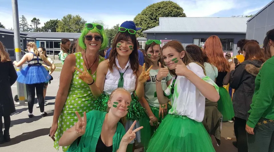 Un gruppo di studentesse della Avonside Girls' High School posa davanti ad edifici e alberi con outfit verdi e a pois.