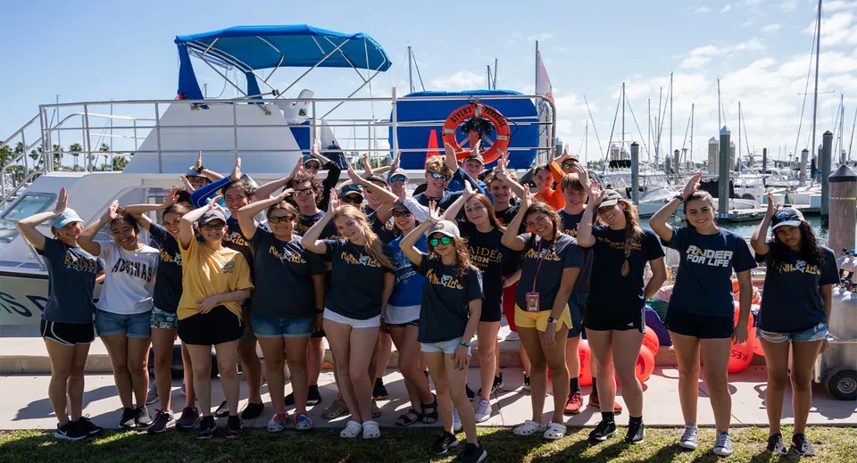 Studentesse della St. Thomas Aquinas High School posano in divise sportive coordinate davanti a un porto turistico con imbarcazioni.