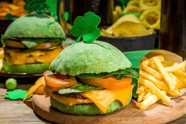 Hamburguesas con pan verde y queso acompañadas de patatas fritas sobre una tabla de madera