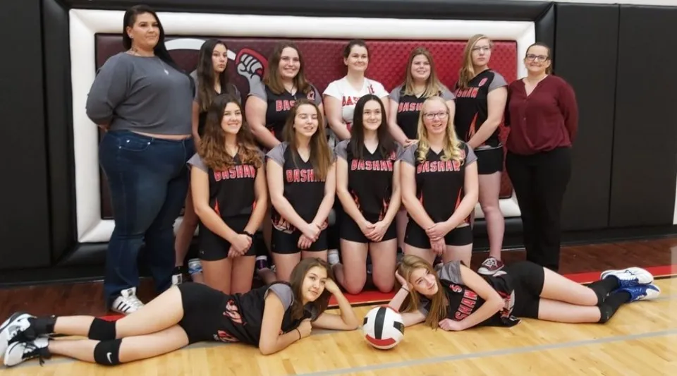 Un gruppo di studentesse della Bashaw School posa insieme come squadra di pallavolo in un parco giochi in legno.
