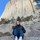 Studentessa sorridente seduta sulle rocce davanti a una grande formazione rocciosa all'estero
