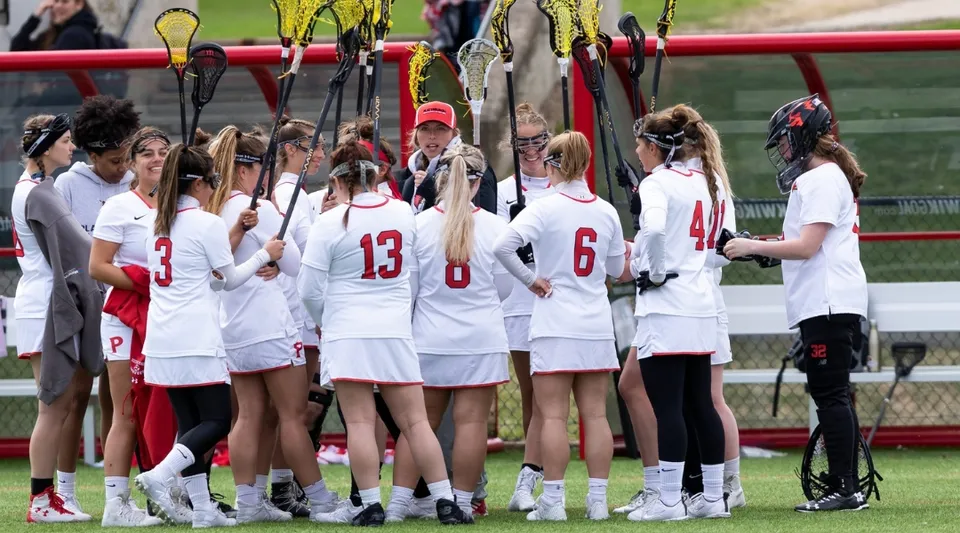 Un gruppo di giovani atlete si trova sul campo sportivo della SUNY Plattsburgh in maglie bianche numerate.
