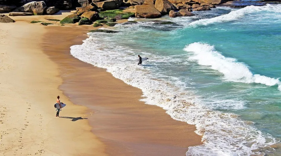 Due persone camminano lungo la spiaggia tra scogliere e onde vicino all'Atwell College.