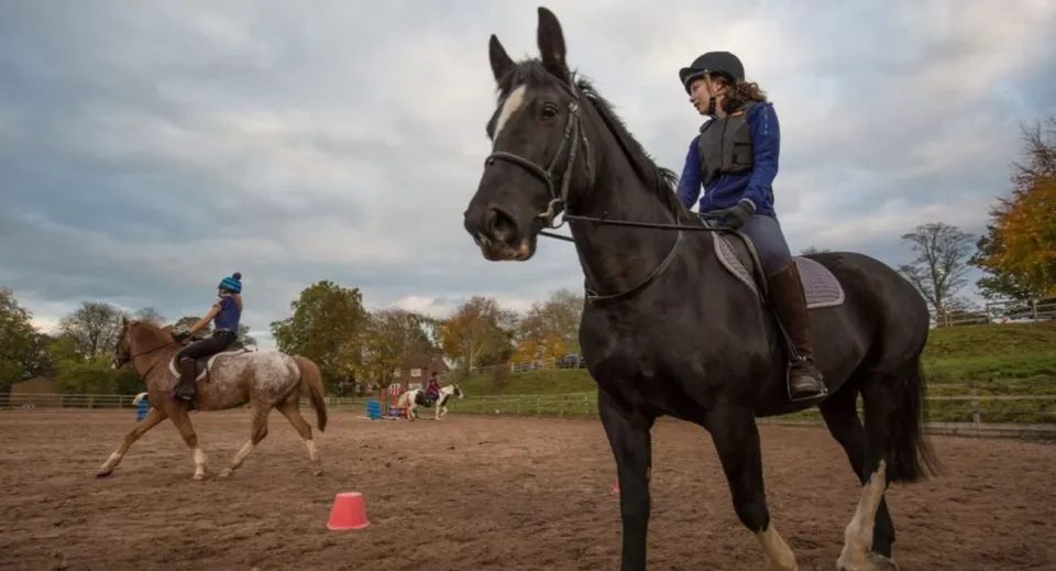 Studentesse della Abbotsholme School cavalcano su un campo da equitazione all'aperto.