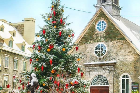 Gran árbol de Navidad decorado frente a una iglesia de piedra con tejados nevados