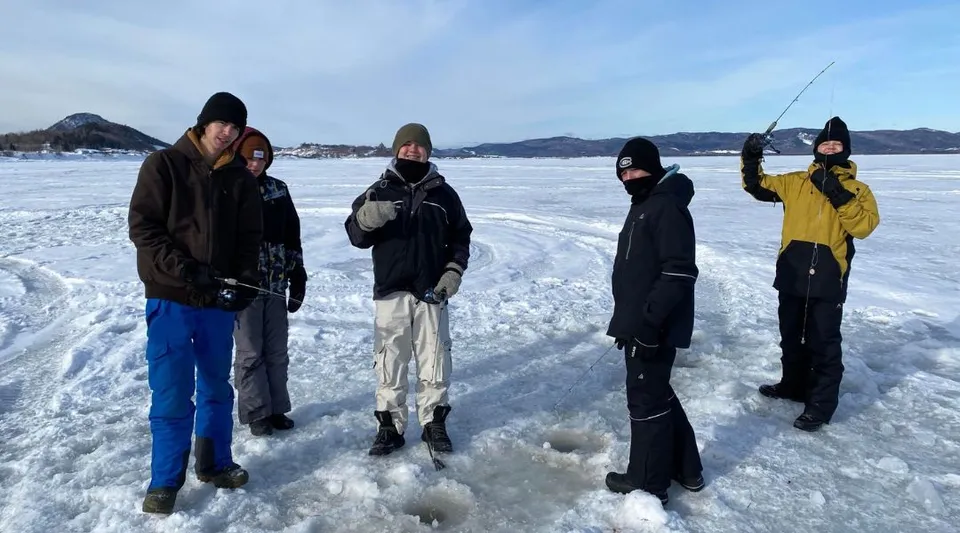 Un gruppo di studenti della Polyvalente Roland-Pépin in abiti invernali si trova su un lago ghiacciato davanti a uno sfondo montuoso.