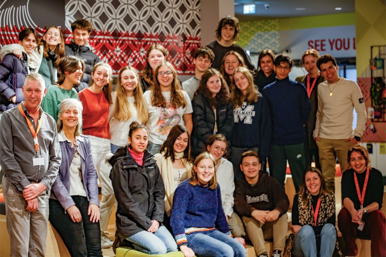 Grande gruppo di studenti in scambio e accompagnatori posano insieme in un ambiente interno