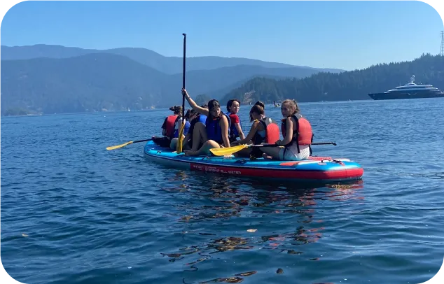 Grupo de alumnos remando juntos sobre una tabla de paddle surf hinchable en un lago rodeado de montañas