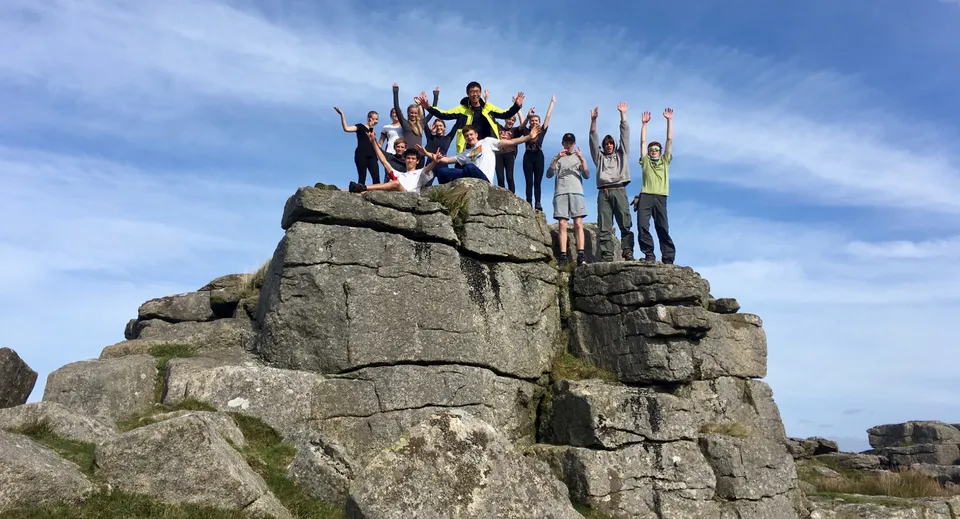 Un gruppo di studenti della Bedales School si trova su una sporgenza rocciosa sotto un cielo blu.