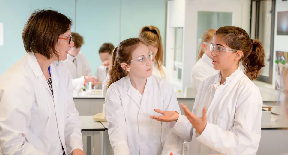 Studentesse della Lewes Old Grammar School discutono in camice bianco in un'aula di laboratorio.