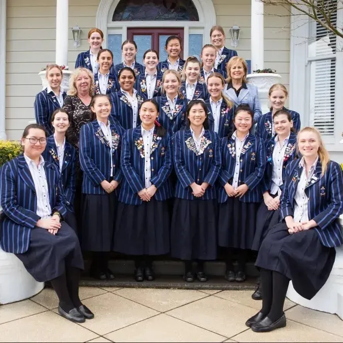 Un grupo de alumnas de la Diocesan School For Girls está con trajes de graduación frente a un edificio con columnas blancas.