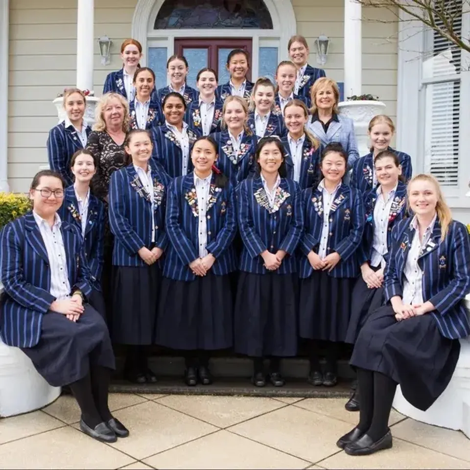 Un gruppo di studentesse della Diocesan School For Girls indossa gli abiti da diploma davanti a un edificio con colonne bianche.