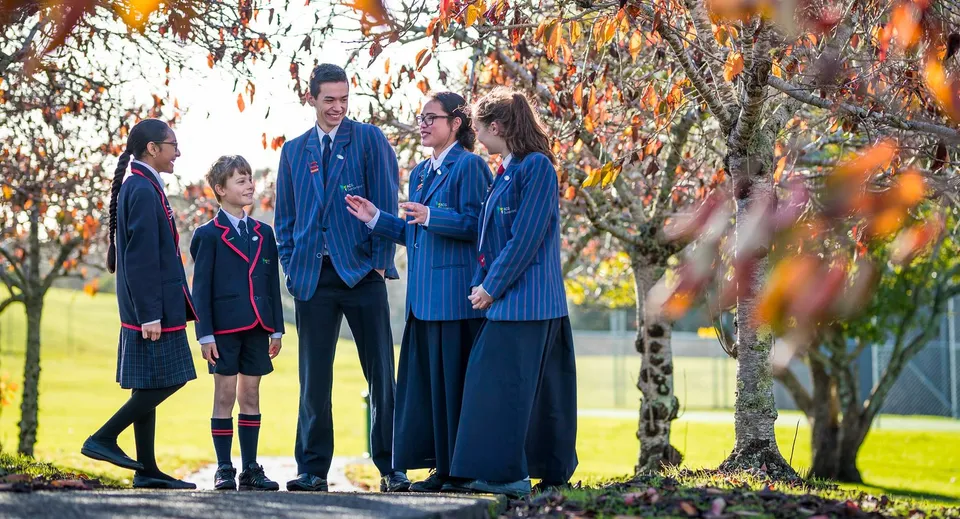 Un gruppo di studenti in uniforme scolastica si trova nel campus dell'ACG Sunderland davanti a una vegetazione autunnale.