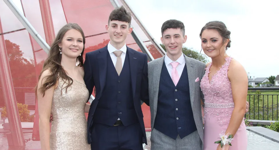 Quattro persone in abito formale sono insieme davanti a un edificio rosso nel campus del Summerhill College.