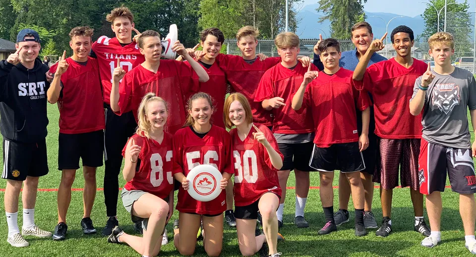 Un gruppo di studenti della Samuel Robertson Secondary School si trova su un campo sportivo con un abbigliamento sportivo rosso.