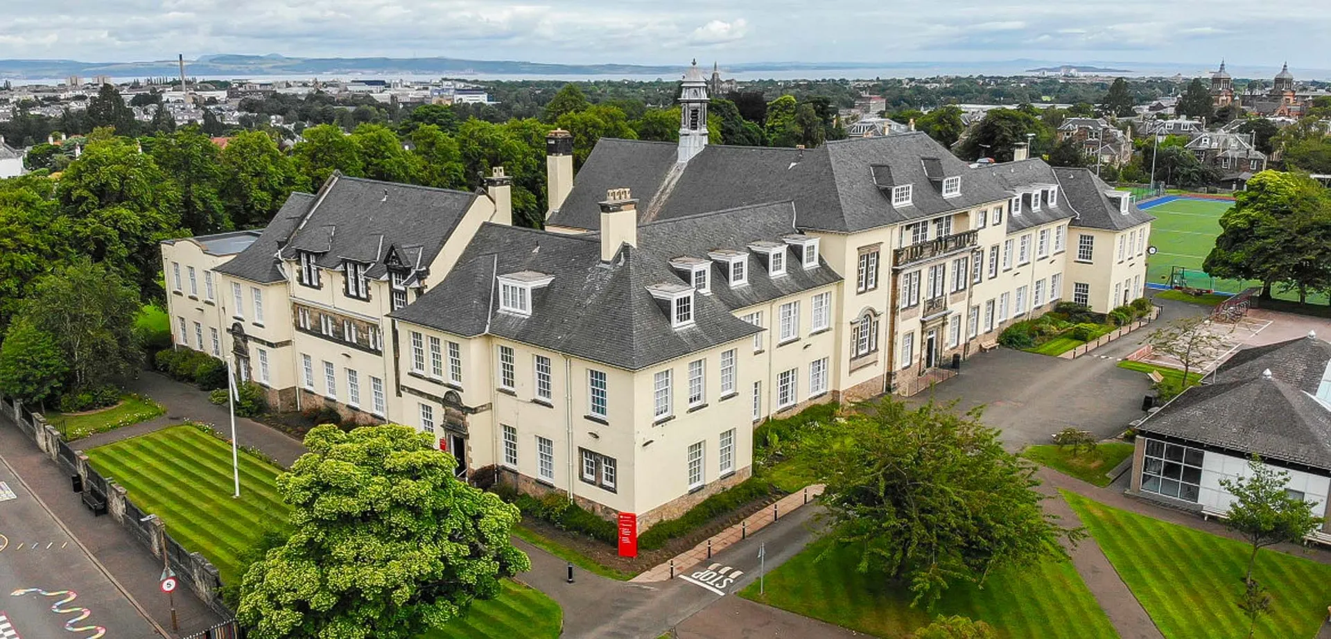 L'edificio principale storico della St. George's School a Edinburgh circondato da alberi con vista sulla città.