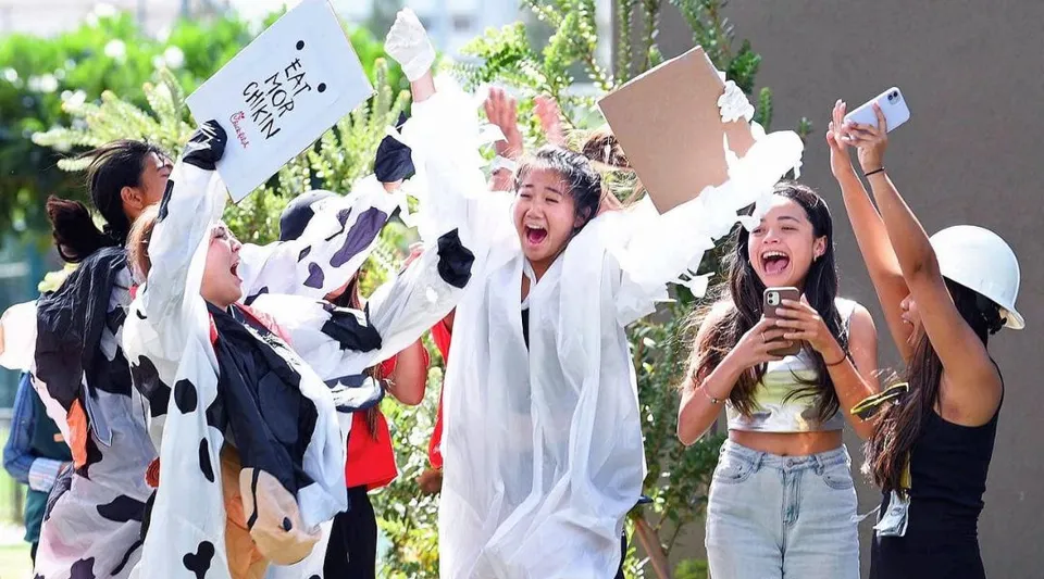 Un gruppo di studentesse della Iolani School tiene in alto dei cartelli all'aperto ed esulta davanti a uno sfondo verde.
